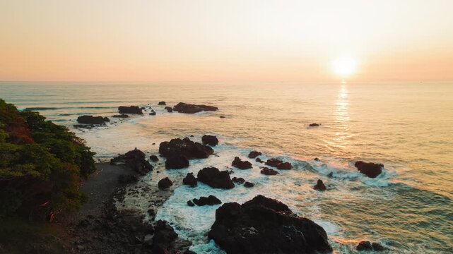 Rocky coastline at sunset with waves and golden sky in Costa Rica pacific shore