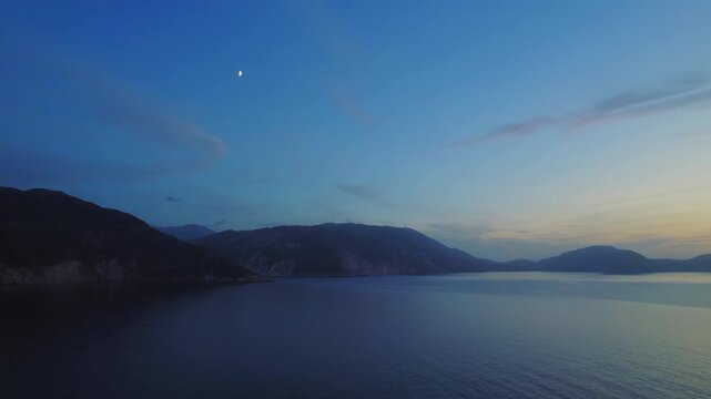 Tranquil evening seascape in Kefalonia with moon above calm bay and distant hills
