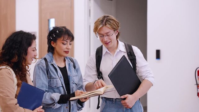 Three diverse university students point to a textbook as a classmate turns pages during a hallway study discussion
