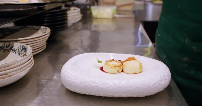 Cooking breakfast. Serving cheesecake. Female restaurant chef hand putting syrnyk dessert on white plate with sweet sauce red jam.