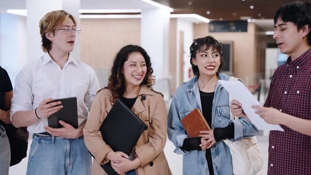 Medium shot of five diverse university students listening as a classmate explains a paper document in a campus hallway