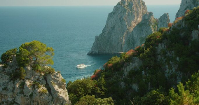 Tour boat gliding between Faraglioni cliffs and turquoise sea near Capri island in high summer