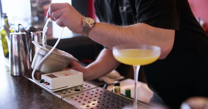 Foaming cocktail. Pub service. Bartender hand making frothy top for drink with professional electronic device on counter with glass.