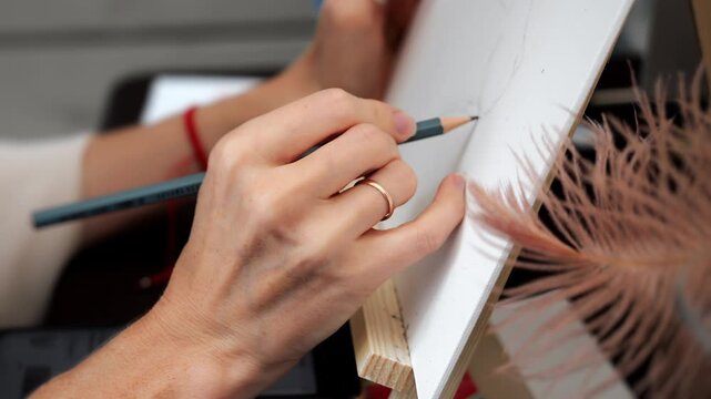 Close-up of female artist hand drawing a preliminary pencil sketch on canvas before painting. Creative process, art class, hobby and artistic education concept.