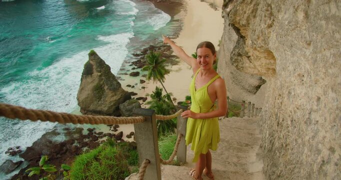 Smiling woman pointing at tropical ocean from cliff steps at Diamond Beach Nusa Penida Bali