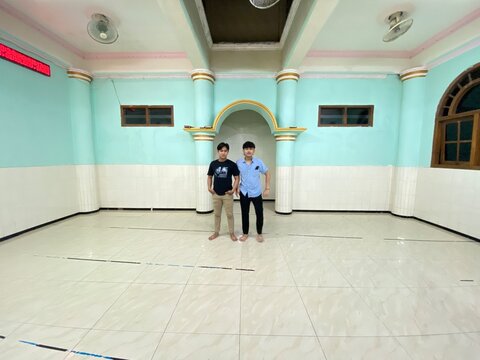 Two men standing inside a spacious hall with light blue and white walls featuring decorative pillars and a clean ceramic tiled floor