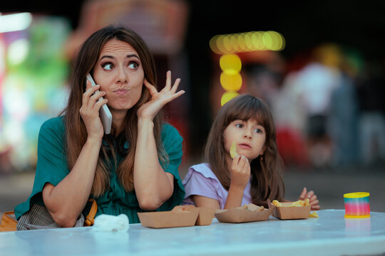 Surprised Mother Covering Her Ears While Talking On Smartphone At Noisy Festival. Stressed young mom blocks loud event noise during mobile phone call near eating child