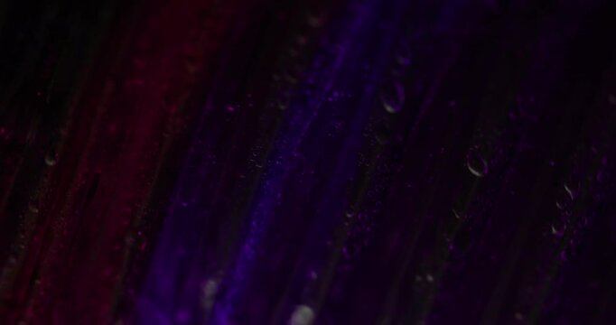Purple drop. Foil background. Defocused vibrant color optical flash twinkle water bubbles on abstract dark black light abstraction.