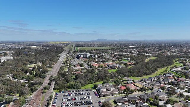 Aerial view of the Werribee train line alongside the winding Werribee River green belt, commuter car parks, and suburban residential neighborhood with local houses in Melbourne, Australia