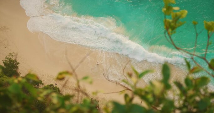 Looking down at white ocean waves washing over sandy shore of Kelingking Bay in Bali Nusa Penida