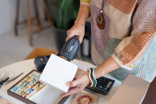 woman scanning product barcode with handheld scanner at handmade retail shop using technology small business management.