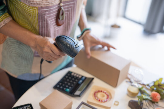 woman scanning product barcode with handheld scanner at handmade retail shop using technology small business management.