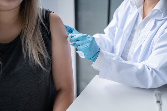 Female doctor administering injection into upper arm of Asian female patient during medical treatment at healthcare clinic.
