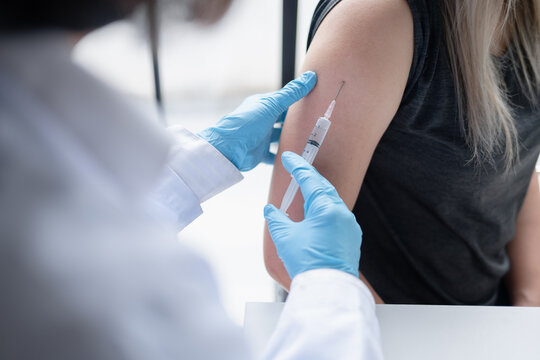 Female doctor administering injection into upper arm of Asian female patient during medical treatment at healthcare clinic.