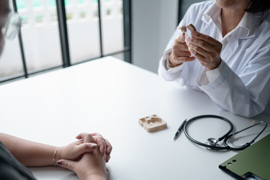 Doctor explaining how to use hearing aid to Asian female patient during hearing care consultation at medical clinic