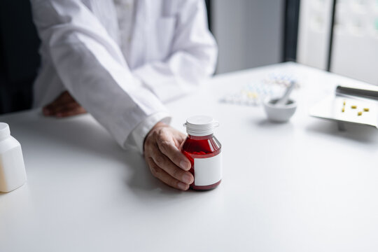 Asian senior female pharmacist handing prescription medicine bottle to customer at pharmacy counter.
