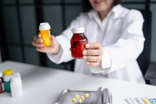 Asian senior female pharmacist handing prescription medicine bottle to customer at pharmacy counter.