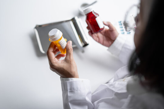 Asian senior female pharmacist reading prescription medicine label representing medication safety pharmaceutical care and modern healthcare.