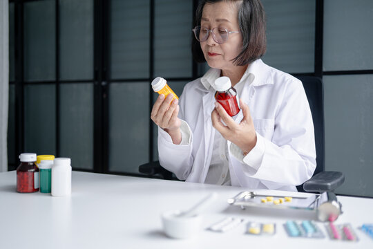 Asian senior female pharmacist reading prescription medicine label representing medication safety pharmaceutical care and modern healthcare.