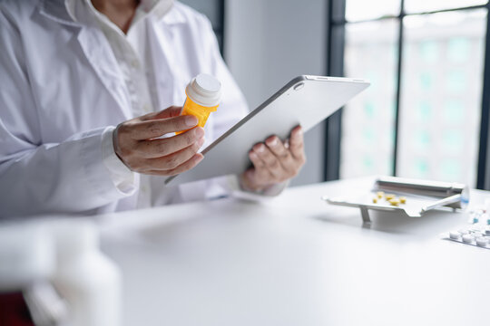 Asian senior female pharmacist using digital tablet representing modern pharmacy pharmaceutical care healthcare technology and medication safety.