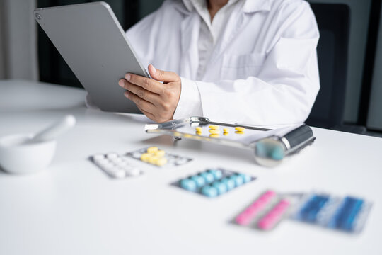 Asian senior female pharmacist using digital tablet representing modern pharmacy pharmaceutical care healthcare technology and medication safety.