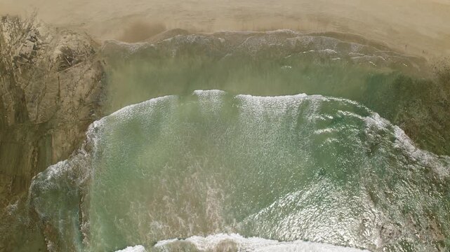 Aerial view of gentle sea waves approaching sandy tropical beach on sunny day