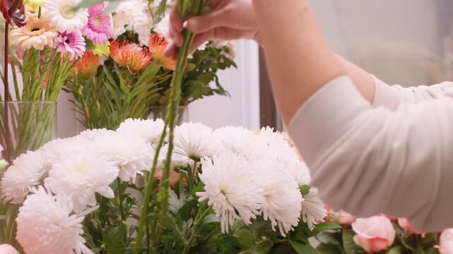 Floral store. Arranging fresh flowers. Unrecognizable professional female hands with seasonal eustoma white color bloom chrysanthemum.