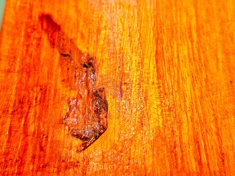 Close-up of vibrant orange wood grain texture with natural knot defect