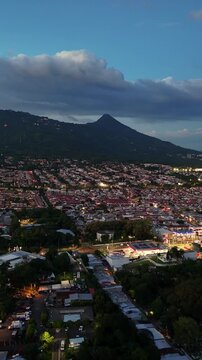 Vista panor&aacute;mica del volc&aacute;n de San Salvador con un cielo azul y nubes sobre el cono rodeado de la ciudad de Santa Tecla en El Salvador formato vertical