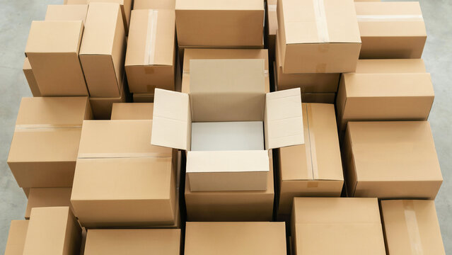 top view of open cardboard box surrounded by stacked shipping boxes
