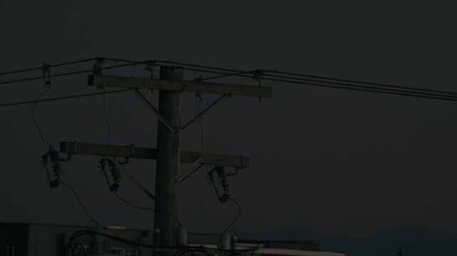 Silhouetted Utility Pole and Power Lines Against Dark Night Sky