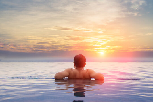 Man relaxing in infinity pool looking at ocean horizon during golden sunset. Vacation and wellness concept. Human-created, not AI.