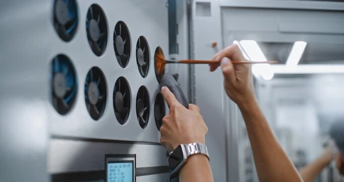 Maintenance of Server Rack Fan Assembly. IT Specialist Vacuums Accumulated Dust From Cooling Fan Intakes Near Digital System Monitors, Preventing Thermal Throttling and Enterprise Hardware Damage.
