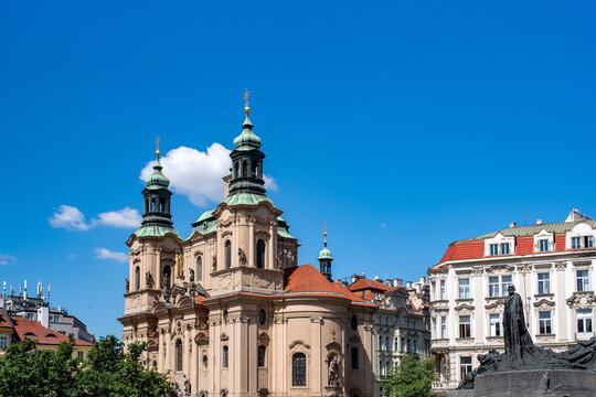 Church of St. Nicholas and Jan Hus Memorial in Old Town Square, Prague, Czech Republic, surrounded by historic architecture under a vivid blue spring sky.