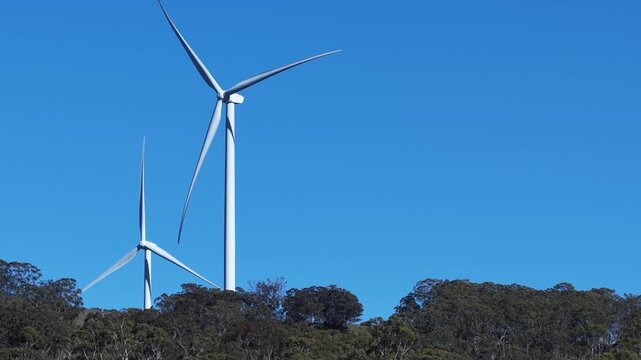 Wind Turbines Rotating Above Forested Ridge Under Clear Blue Sky