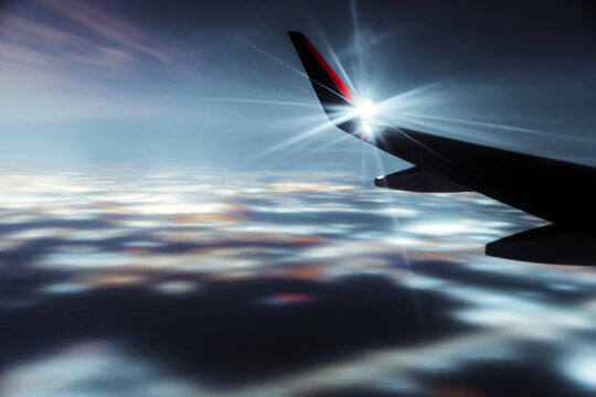 Wing of plane flying in sky above clouds at dawn. Travel, transport concept