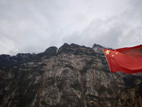 The Chinese national flag waves boldly before the rugged vertical cliffs of Sichuan&rsquo;s monumental Dadu River Jinkou Grand Canyon.