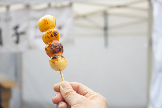 Girl's hand holds a mitarashi dango or Japanese rice cake dumpling skewer. Kumamoto, Kyushu, Japan