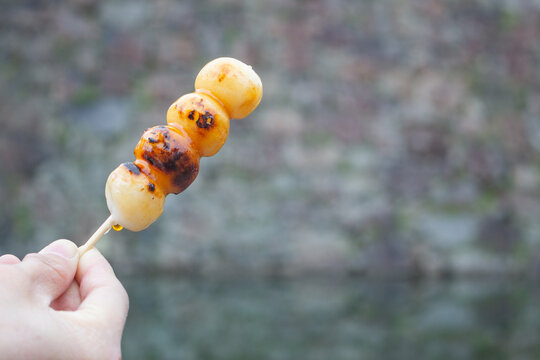 Girl's hand holds a mitarashi dango or Japanese rice cake dumpling skewer. Kumamoto, Kyushu, Japan