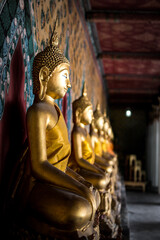Row of golden Buddha statues along the gallery wall in a Thai temple, Bangkok, Thailand © Natthawat