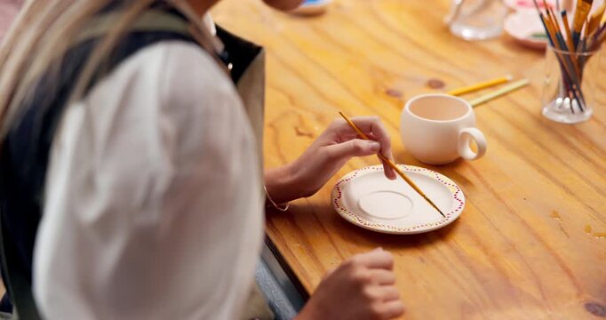 Woman, hands and painting in art studio with ceramic plate, DIY and workshop for skill development. Artist, person and creativity in pottery class with paintbrush, craft tools and color for project.