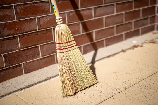 Straw Broom Leaning Against Brick Wall