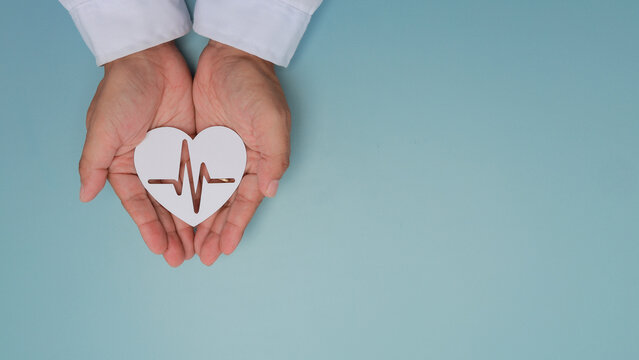 Doctor hand holding paper heart pulse showing compassionate caregiving concept and hopeful healthcare support on blue background