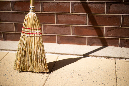 Traditional Straw Broom Against Red Brick Wall