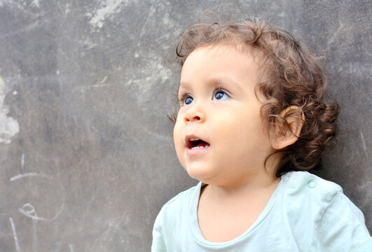 Hispanic toddler looking up with opened mouth.