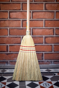 Traditional Straw Broom Against Brick Wall