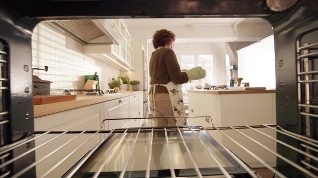 Oven point of view shows a woman wearing oven mitts removing a freshly baked apple pie and carrying it to the kitchen counter.
