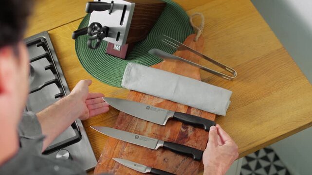 Overhead view of a person taking out several kitchen knives and arranging them on a wooden cutting board before food preparation.