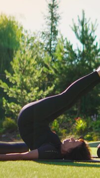 Woman practicing advanced outdoor yoga inversion pose on grass mat in sunny garden, stretching legs and spine while relaxing and focusing on mindful breathing