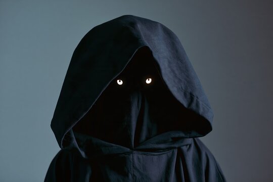 Eerie shadow monster figure in a dark hooded cloak with glowing eyes for Halloween celebration